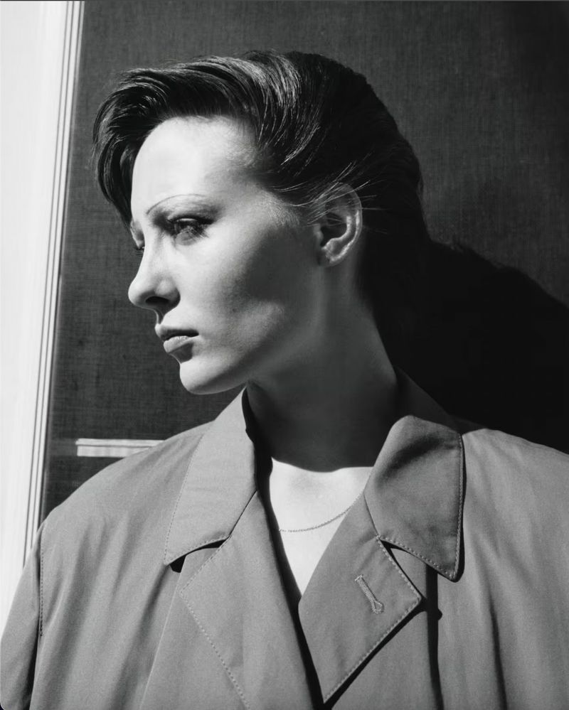 Monochrome portrait of adult woman in profile with short hair wearing a collared coat in front of a window with natural lighting.