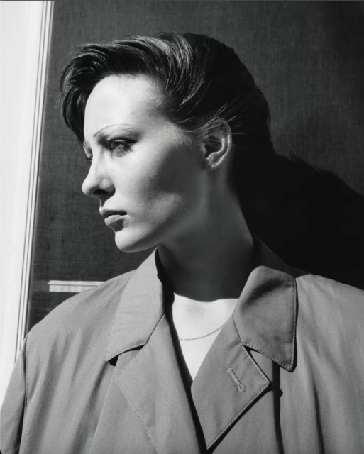 Monochrome portrait of adult woman in profile with short hair wearing a collared coat in front of a window with natural lighting.