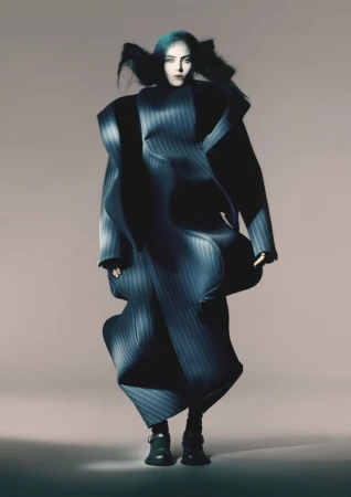 A model wearing a large, pinstripe coat-dress stands in a photo studio with neutral backdrop, showcasing fashion and editorial photography.