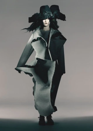Fashion model in houndstooth jacket and long skirt with dramatic hat, studio shot, monochromatic aesthetic. Runway fashion concept.