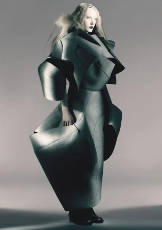 Model wearing sculptural avant-garde charcoal grey architectural fashion design against a plain grey background