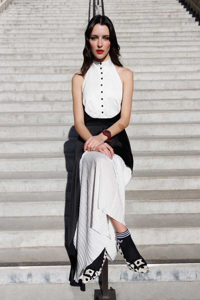 Fashionable woman with red lipstick, wearing a monochrome top and long skirt, sits on concrete stairs in an eye-level medium shot.