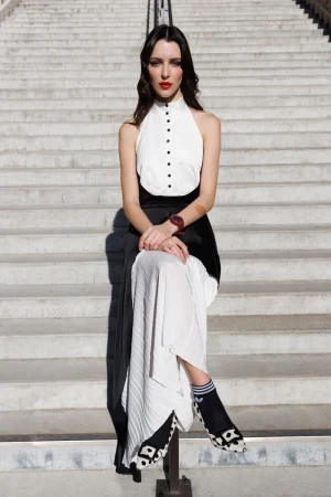Fashionable woman with red lipstick, wearing a monochrome top and long skirt, sits on concrete stairs in an eye-level medium shot.
