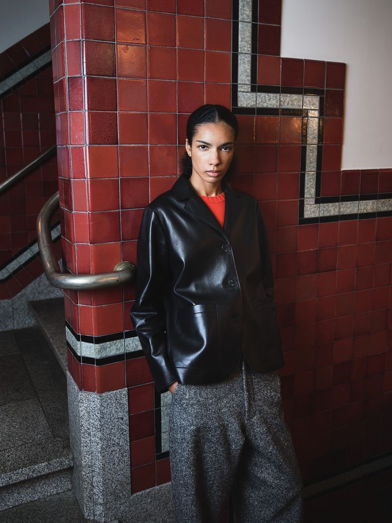 Fashionable woman in a black jacket poses against red-tiled stairs, creating a stylish portrait with a blend of texture and color.