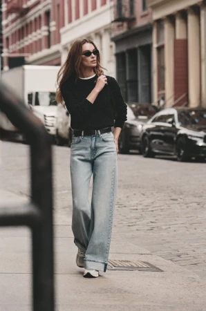 Model in black sweater and light wash jeans walking down a city street for Mavi Fall 2025 Editorial
