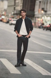 Male model wearing dark shirt over white t-shirt and jeans standing on a city street.