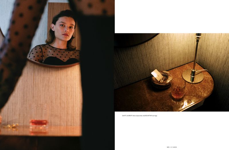 Woman with dark hair reflected in a mirror wearing a black polka dot mesh top, next to an end table with a lamp and glass.
