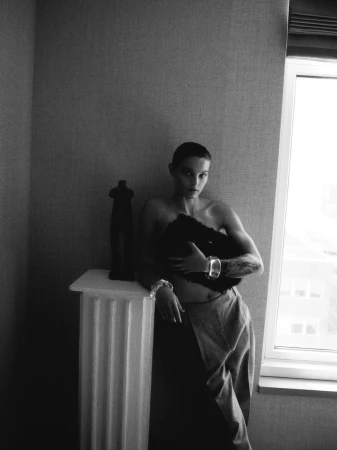 Black and white portrait of a short-haired adult female posing in front of a window with a column-shaped table in an indoor setting.