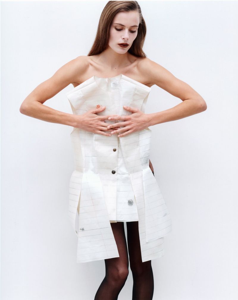 Model Lydia-Angel posing in a structured strapless white mini dress and black sheer tights against a white studio background.