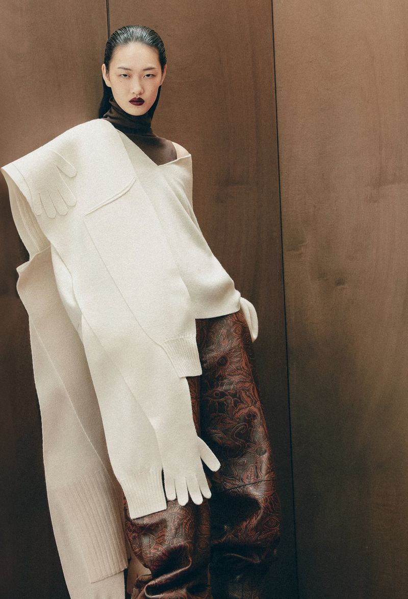 Asian woman in editorial fashion portrait with a white knit shawl, brown turtleneck, and glossy brown reptile-patterned trousers.