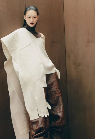 Asian woman in editorial fashion portrait with a white knit shawl, brown turtleneck, and glossy brown reptile-patterned trousers.