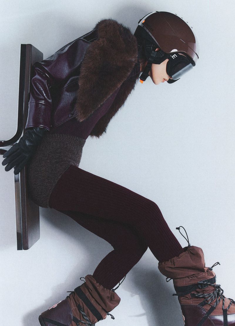 Woman in ski helmet and boots poses in a stylish outfit against a stark background, fashion photography, studio shot.