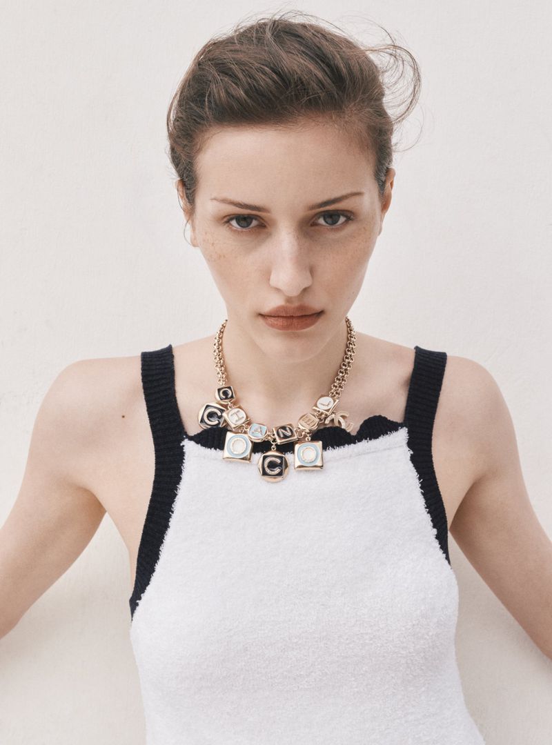 Portrait of an adult woman with freckles wearing a necklace, white dress, and natural makeup in a brightly lit neutral environment.