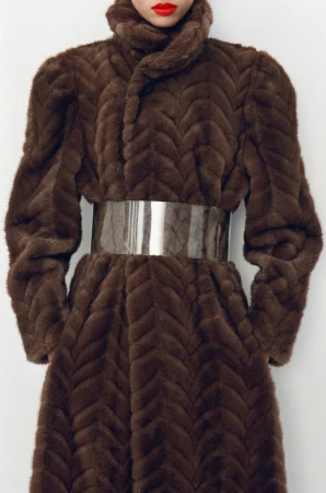 Elegant woman in a brown herringbone pattern mink coat with an oversized silver belt and bold red lipstick, against a plain white background.