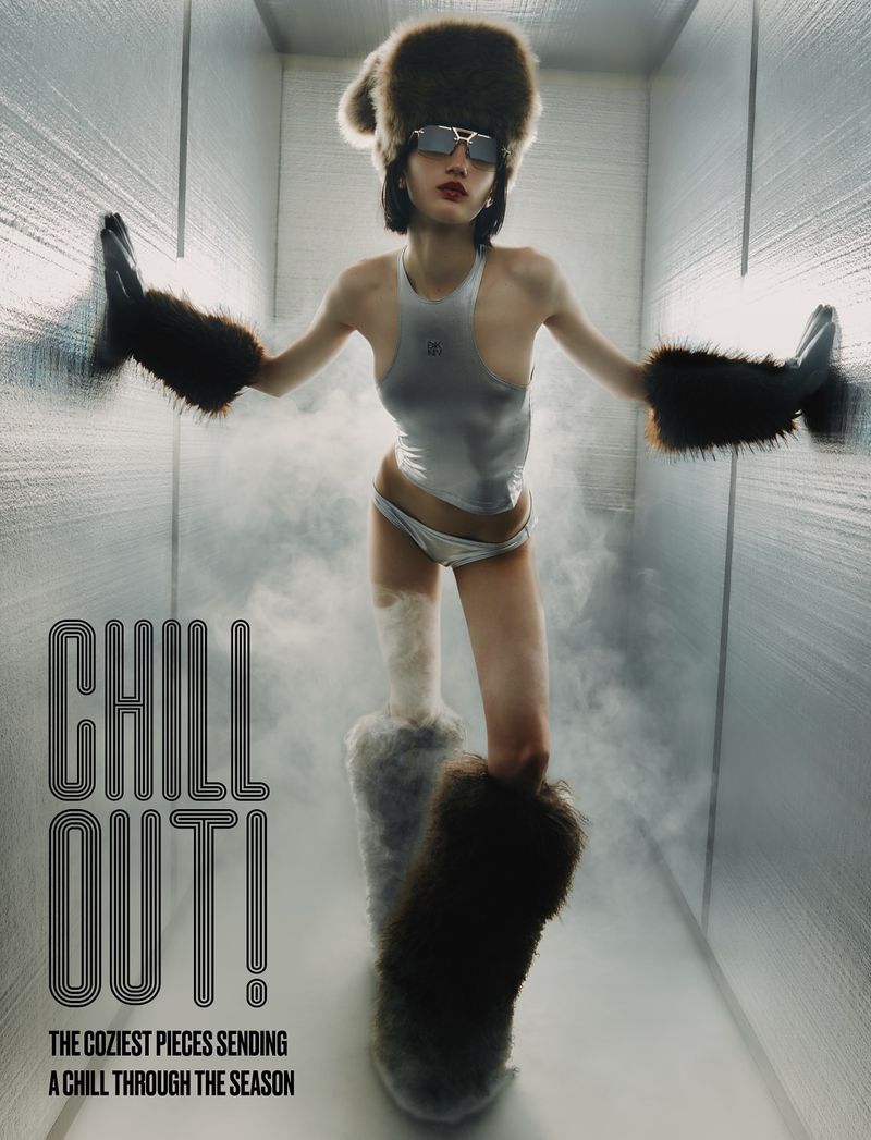 Fashion editorial shot of woman wearing silver swimsuit and furry hat, arm warmers, and boots in a brightly lit corridor with fog.