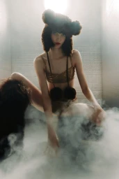 Model wearing a fuzzy brown earflap hat and metallic gold bikini top in a smoky setting for V Magazine