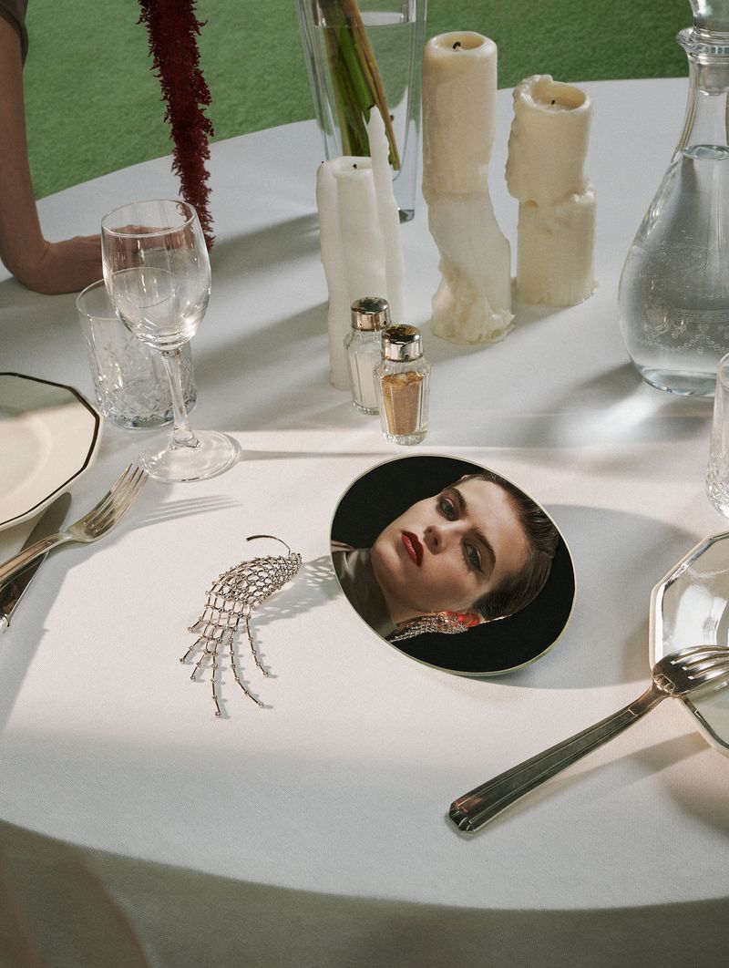 Elegant table setting with reflective portrait plate, modern silverware, candles, and glassware against a bright green backdrop.