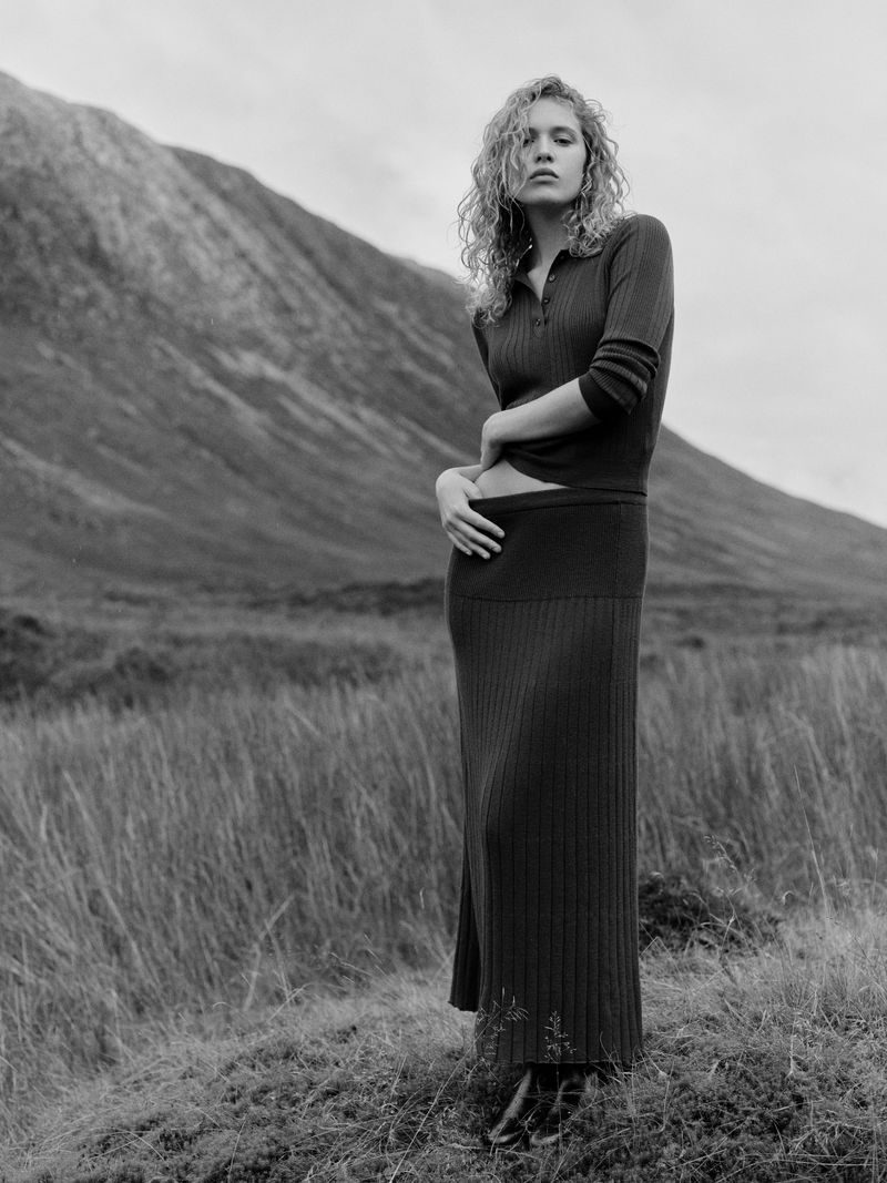 Model Liv Walters posing in a ribbed knit top and maxi skirt outdoors against a mountain slope in Scotland.