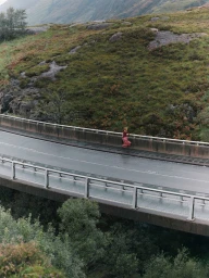 Model walking across a concrete bridge set against a lush green mountain landscape in Scotland