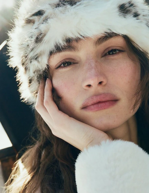 Close-up portrait of an adult female with fair skin and brown hair, wearing a faux fur hat and jacket in natural sunlight.