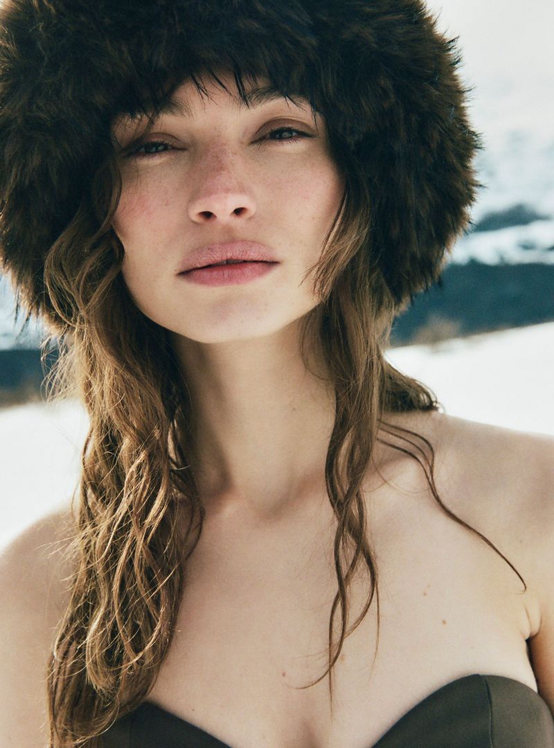Close-up of a woman wearing a fur hat in a snowy landscape. The model poses, capturing fashion and beauty in a natural setting.