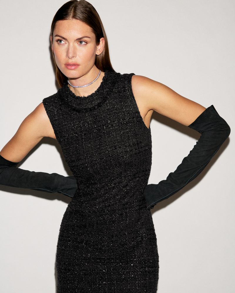 Model wearing a sleeveless black tweed dress paired with long black opera gloves and a sparkling choker against a light studio backdrop.