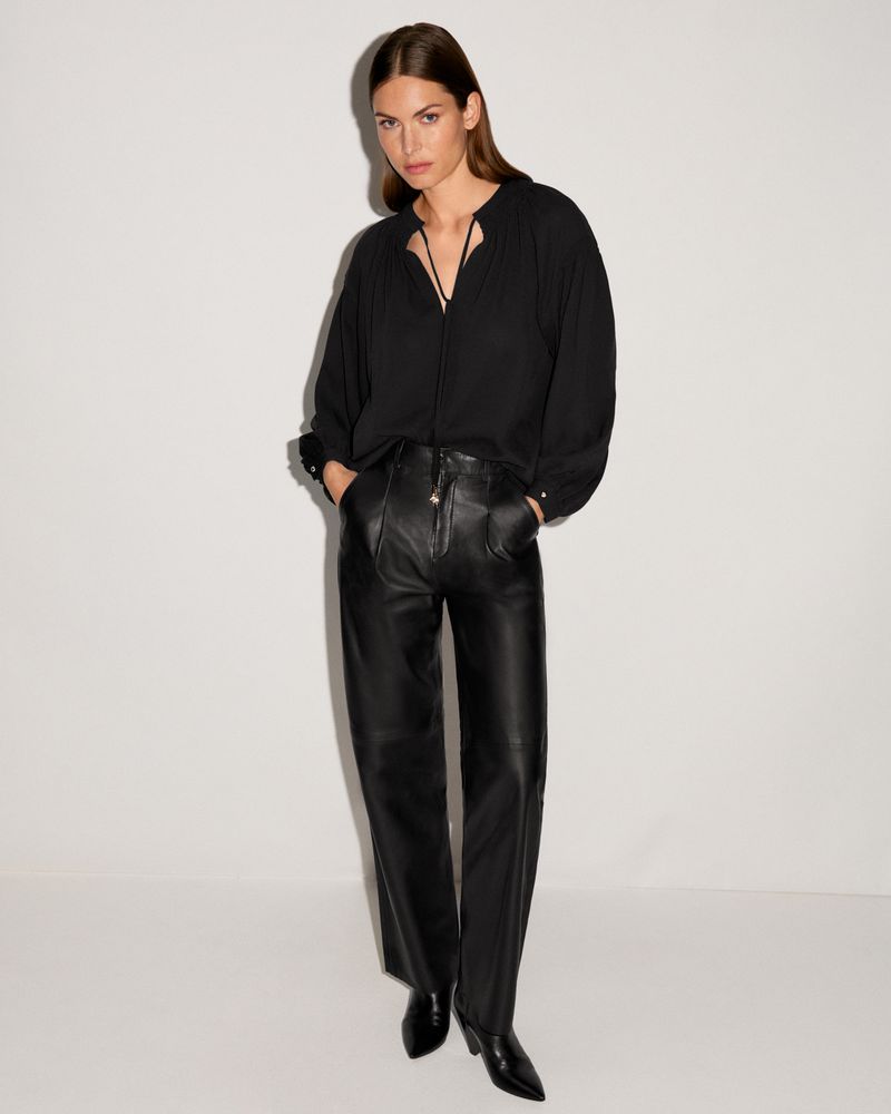Full shot of a woman in a black blouse and leather pants. The outfit is posed against a white backdrop in a fashion shoot.