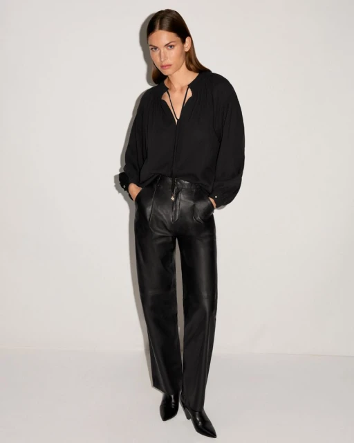 Full shot of a woman in a black blouse and leather pants. The outfit is posed against a white backdrop in a fashion shoot.
