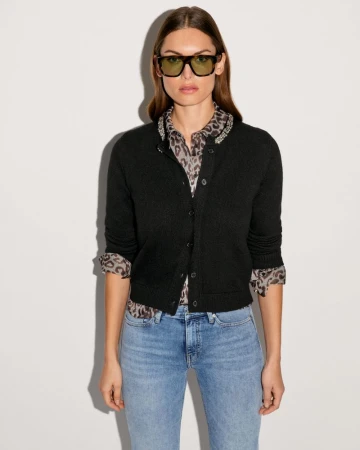 Model wearing dark sunglasses, a black cardigan over an animal-print shirt, and blue jeans against a plain white background.