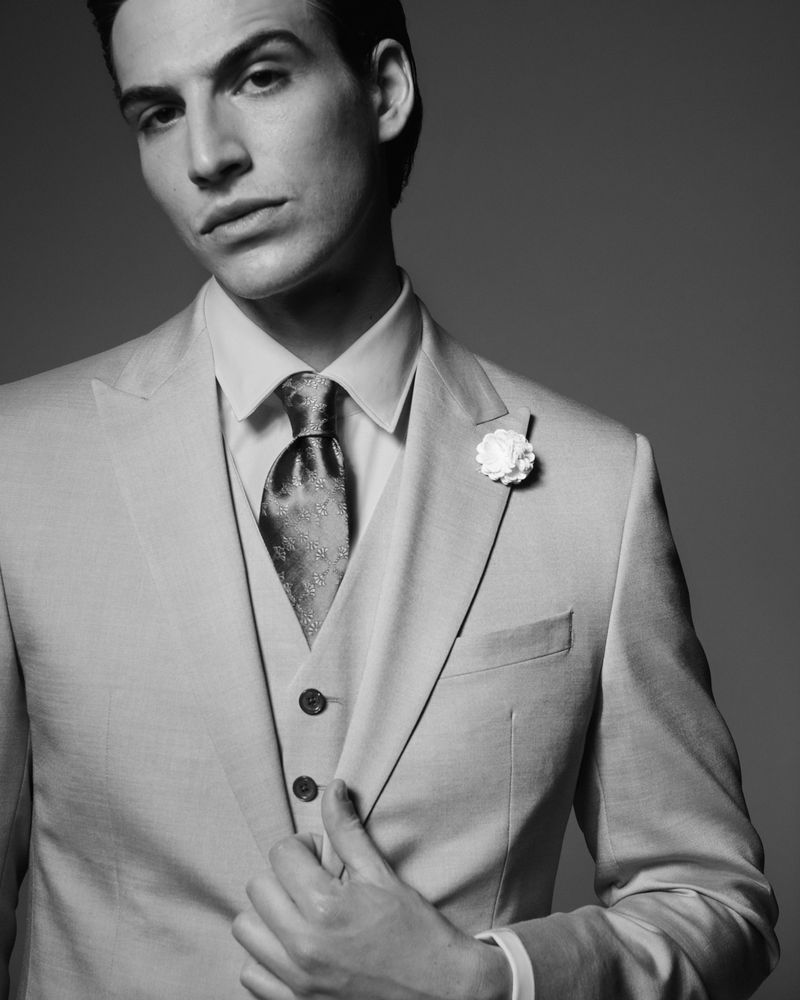 Monochrome studio portrait of a handsome adult male in a tailored suit with a patterned tie and boutonniere, showcasing formal fashion.
