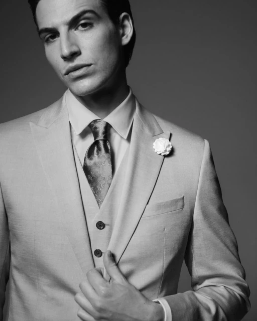 Monochrome studio portrait of a handsome adult male in a tailored suit with a patterned tie and boutonniere, showcasing formal fashion.