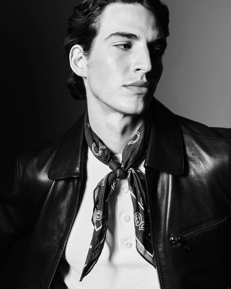 Black-and-white portrait of an adult male wearing a leather jacket and neckerchief, lit with dramatic studio lighting.