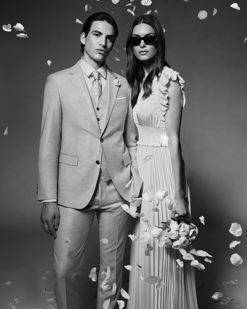 Monochrome portrait of a fashionable couple posing amidst falling rose petals, the man in a suit and the woman in sunglasses.