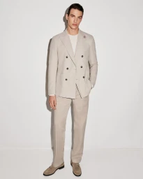 Model Amerigo Valenti in a light beige double-breasted suit and suede loafers standing against a plain white studio background.