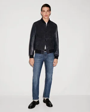 Model Amerigo Valenti wearing a dark bomber jacket, blue denim jeans, and black loafers against a light studio backdrop.