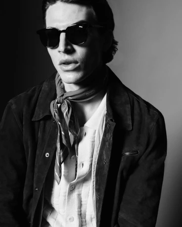 Model Amerigo Valenti wearing dark sunglasses, a tied neck scarf, and an open dark jacket in a black and white studio portrait for JOOP!.