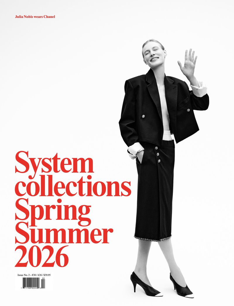 Fashion editorial shot of a woman in a black skirt suit, smiling and waving on a white background, with red sans-serif text.