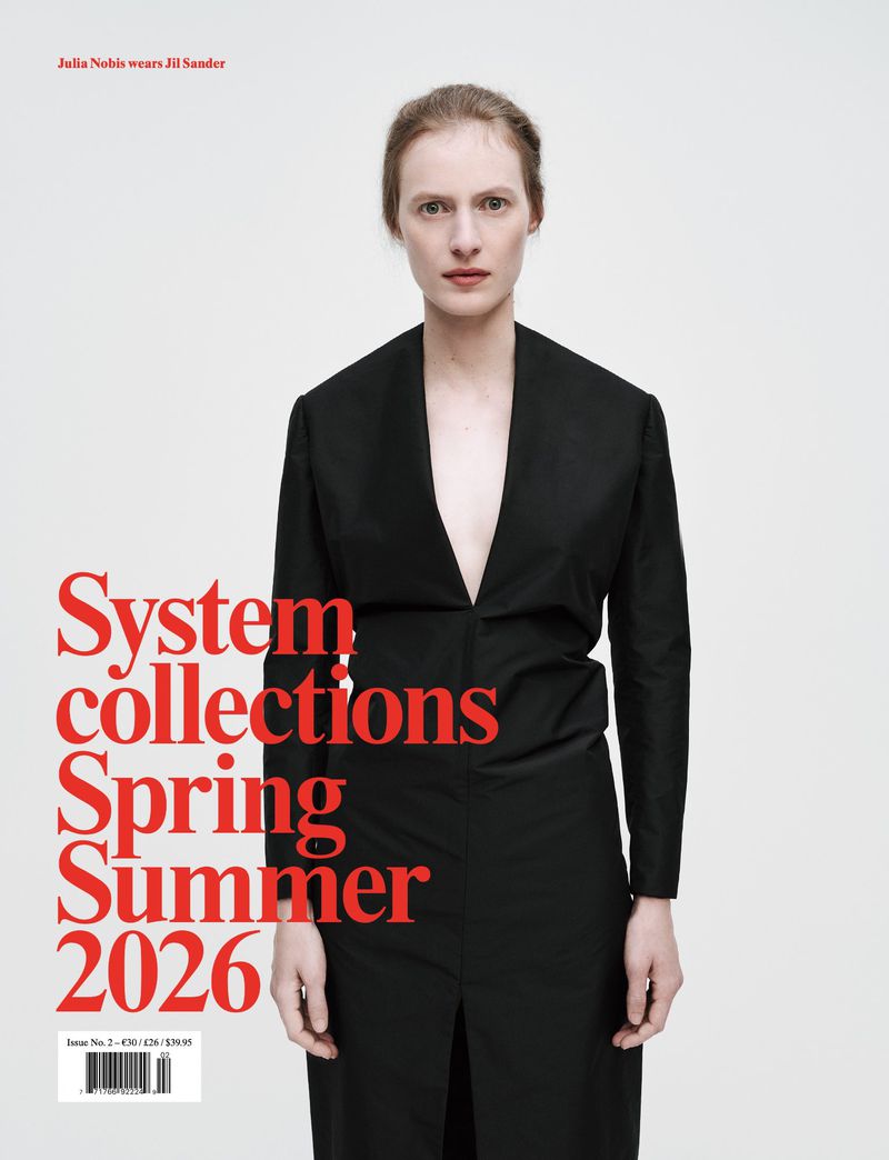 Fashion magazine cover with a model wearing a black blazer dress against a white background with red typography and clean studio lighting.