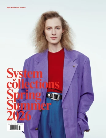 Editorial fashion shot of a blonde adult female wearing a purple blazer, red shirt, and blue pants against a bright white backdrop.