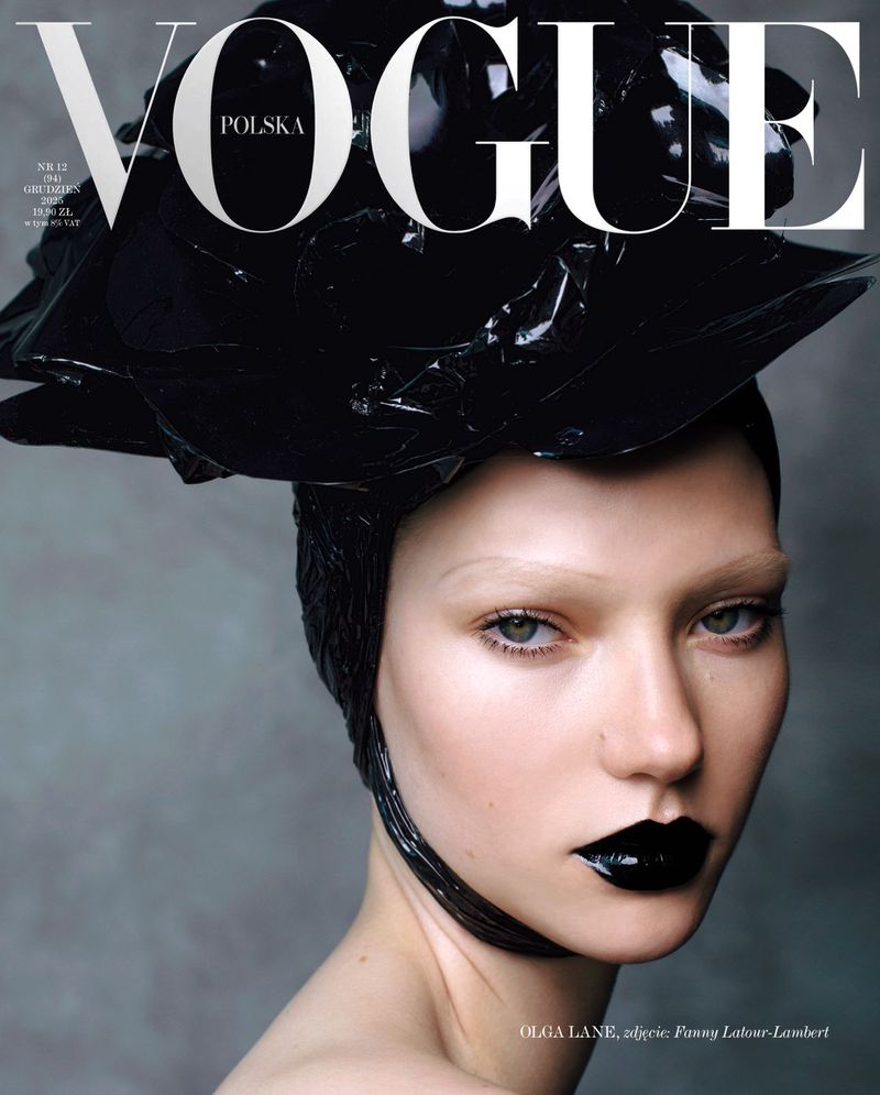 Vogue Polska cover featuring a woman with pale skin, glossy black lipstick, and a large, shiny black headpiece, on a gray background.