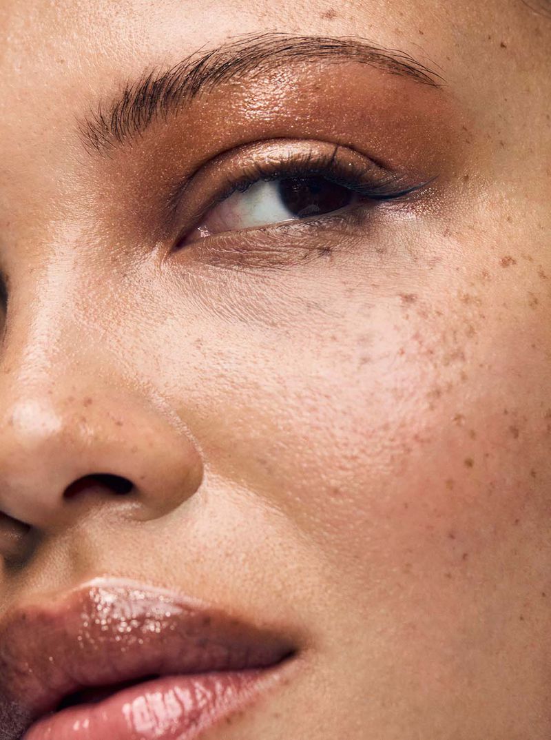 Close-up of a woman's face with warm-toned eyeshadow, glossy lips, and freckles highlighting her natural beauty and makeup.