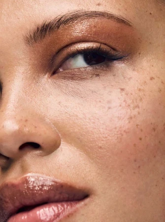 Close-up of a woman's face with warm-toned eyeshadow, glossy lips, and freckles highlighting her natural beauty and makeup.