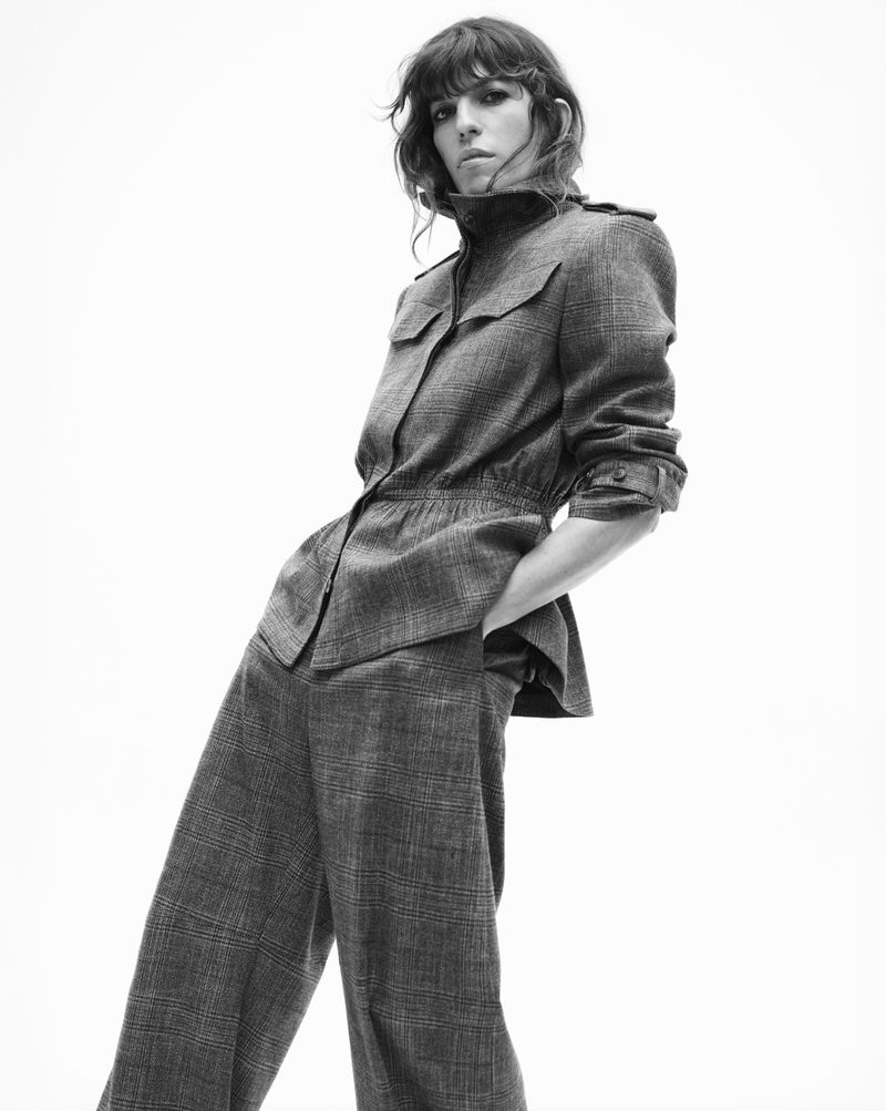 Black and white portrait of a woman in patterned pantsuit looking at the camera in a bright photo studio on a white background.