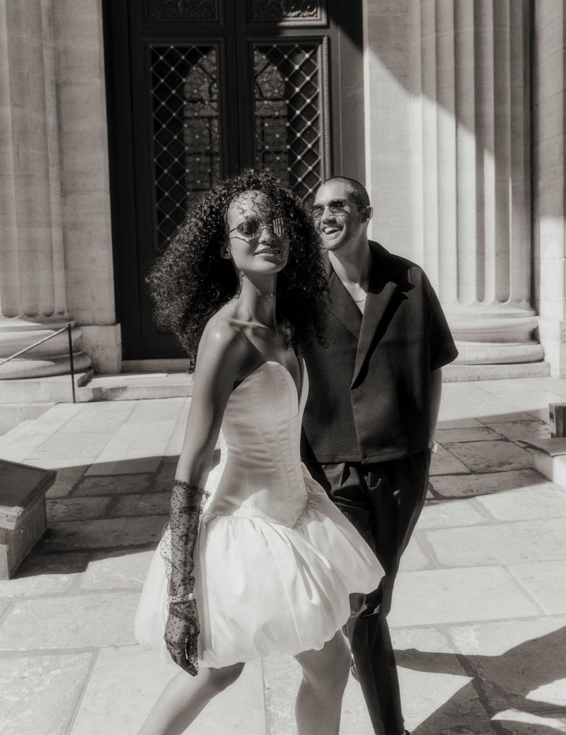 A stylish couple stands outside a building with large pillars in this high-contrast black and white fashion shot with high-fashion attire.