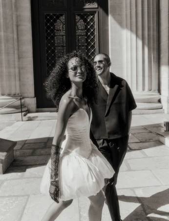 A stylish couple stands outside a building with large pillars in this high-contrast black and white fashion shot with high-fashion attire.