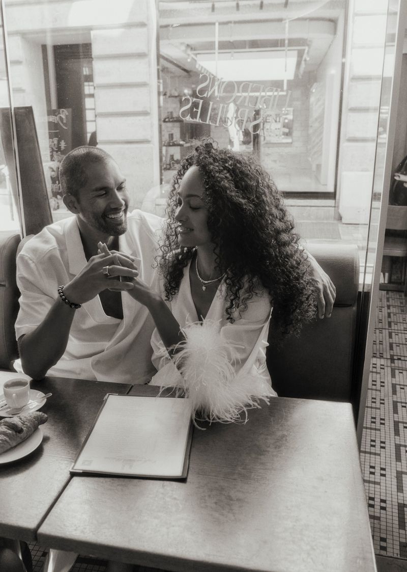 A stylish biracial couple sitting at a cafe table with coffee and a croissant, enjoying an intimate moment in a European setting in black and white.