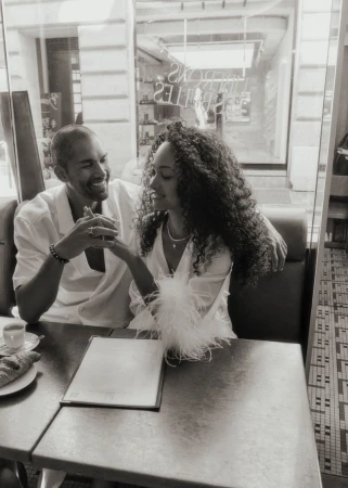 A stylish biracial couple sitting at a cafe table with coffee and a croissant, enjoying an intimate moment in a European setting in black and white.