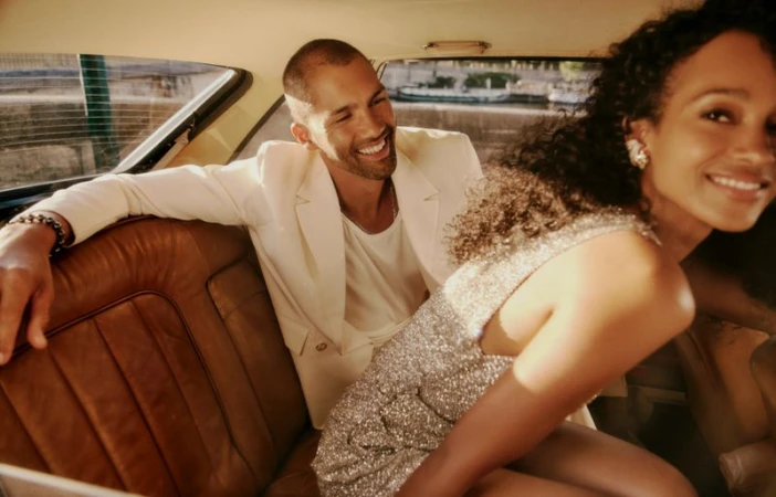 Smiling man and woman in a classic car with leather seats. The woman wears a shimmering dress, and the man wears a white suit jacket.