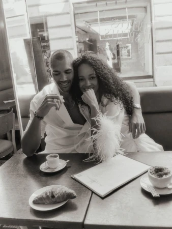 A man and woman sitting together at a cafe table with coffee and croissants, captured in a monochromatic editorial style.