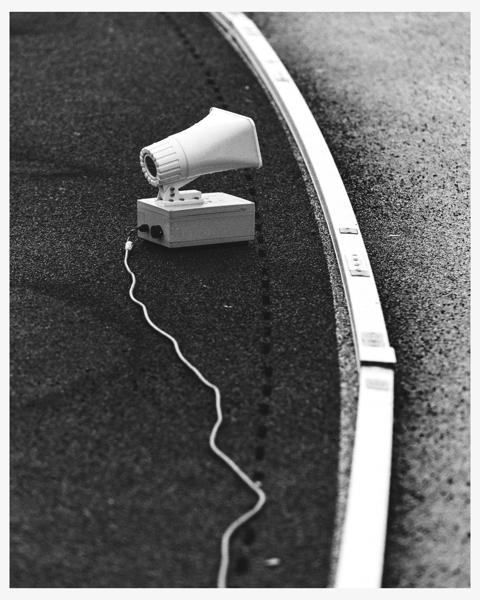 Vintage black and white photo of a megaphone speaker and cable on a speckled surface next to a track-like border in a monochromatic image.